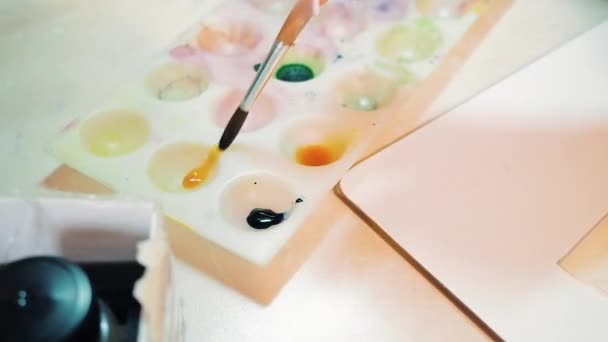 Mujeres manos mixtas pintura acrílica cepillo suave. Gouache se mezcla en una paleta de plástico blanco. Disparar un vídeo de primer plano con el efecto de disparar con las manos — Vídeo de stock