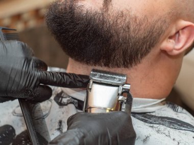 Erkekler sakal kesme makas ve siyah tarak ile, yakın görünümü. Siyah lastik eldivenler içinde stilistli eller. Kuaför lük teshasında usta. Seçici yumuşak odak. Bulanık arka plan.