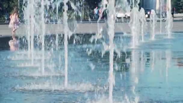 Wasserstrahlen verändern Höhe und Druck. Städtische Szene eines heißen Sommertages in der Nähe eines trockenen Brunnens. kleines Mädchen, das am Brunnenrand spielt. verschwommener Hintergrund, weicher Fokus. Menschen gehen im Hintergrund — Stockvideo