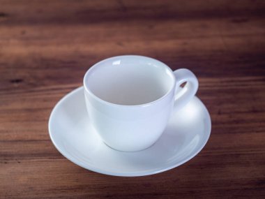 Ahşap masa üzerinde boş kahve fincanı, yakın görünümü. Beyaz fincan ve tabak kahverengi masada. Renkli arka plan. Seçici yumuşak odak. Bulanık arka plan.