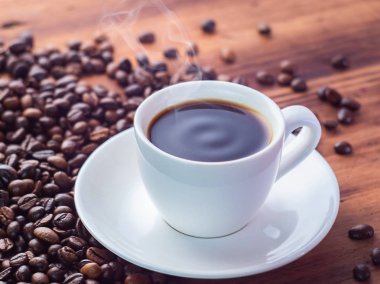 Beyaz kahve fincanında aromatik espresso içmek, yakından bakabilirsiniz. Kavrulmuş kahve çekirdekleri kahverengi masaya haplanmış. Ahşap masa dokusu. Seçici yumuşak odak. Bulanık arka plan.
