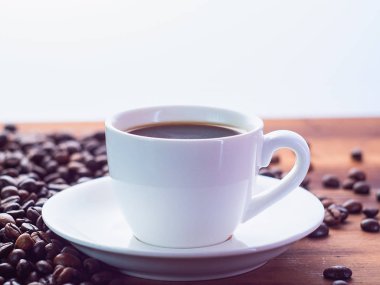 Kahverengi masada espresso ile beyaz kahve fincanı arka plan, yakından görünümü. Kavrulmuş kahve çekirdekleri kahverengi masaya haplanmış. Seçici yumuşak odak. Bulanık arka plan.