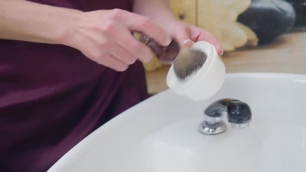 Stylist förbereder raklödder med Rakborste. Händerna på frisör på nära håll. Tvättställ i frisörsalongen på suddig bakgrund. Selektivt mjukt fokus. — Stockvideo