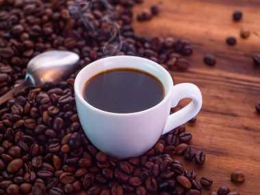 Kahve çekirdekleri çay kaşığı ve beyaz kahve fincanı aromatik espresso dolu kahverengi masaya haplanmış. Ahşap masa dokusu. Seçici yumuşak odak. Bulanık arka plan.