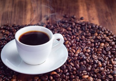 Kavrulmuş kahve çekirdekleri bileşimi yuvarlak beyaz fincan aromatik espresso dolu pilled, yakından görünümü. Kahverengi ahşap masa dokusu. Seçici yumuşak odak. Bulanık arka plan.