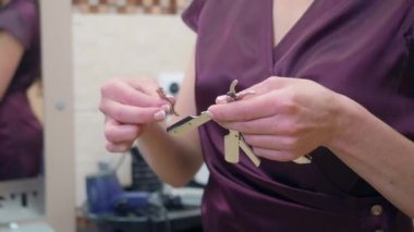 Stilist jilet açmak için bıçak koyar, yakın çekim. Koyu kırmızı üniformalı kuaför tıraş için açık jilet hazırlıyor. Kuaför salonuna kaydedilmiş. Seçici yumuşak odak. Bulanık arka plan.