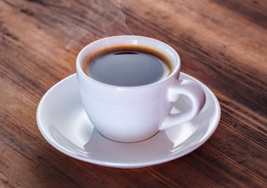 Beyaz fincan kahve içerken yakından bak. Beyaz kahve fincanı ve kahverengi masa üzerinde tabak. Ahşap masa dokusu. Seçici yumuşak odak. Bulanık arka plan.