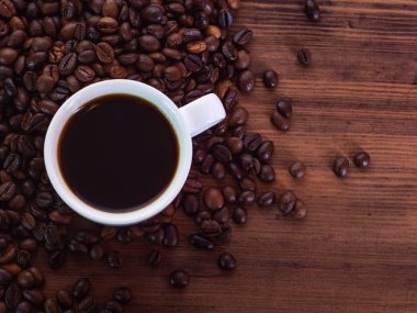 Kahverengi masaya haplanmış siyah espresso ve kahve çekirdekleri dolu beyaz kahve fincanı üzerinde üst görünümü, yakın. Ahşap masa dokusu. Sanat kompozisyonu. Seçici yumuşak odak. Bulanık arka plan.