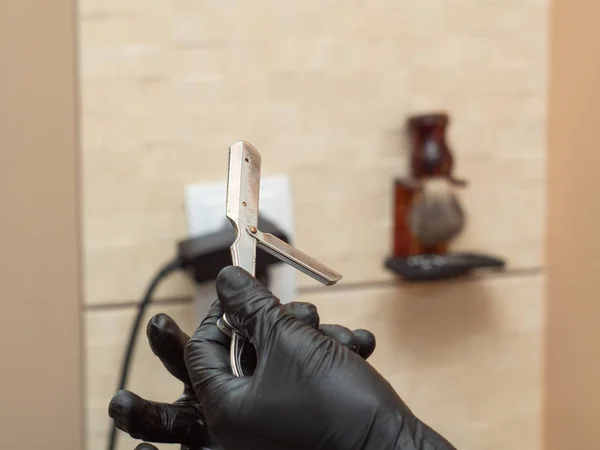 Stylist bereitet offene Rasiermesser für die Rasur, Nahsicht. beherrscht die Hände in schwarzen Gummihandschuhen. Innenraum des Friseursalons. selektiver weicher Fokus. verschwommener Hintergrund. — Stockfoto