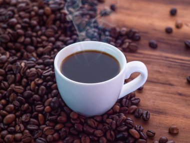 Kahverengi sehpanın üzerine kahve çekirdekleri ve aromatik espresso dolu kahve fincanı, yakın görüş. Ahşap masa dokusu. Seçici yumuşak odaklanma. Bulanık arkaplan.