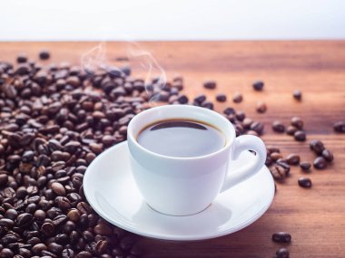 Kahverengi masaya haplanmış doğal kavrulmuş kahve çekirdekleri, yakın görüş. Tahta masada siyah espresso ile beyaz kahve fincanı. Ahşap masa dokusu. Seçici yumuşak odaklanma. Bulanık arkaplan.