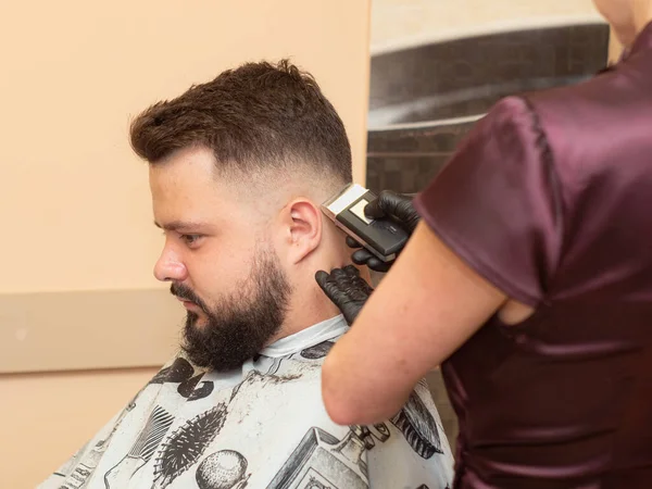 Mujer cortando el pelo de los clientes con clipper, vista de cerca. Estilistas manos en guantes de goma negro. Proceso de peluquería, fotografiado en barbería. Enfoque suave selectivo. Fondo borroso . —  Fotos de Stock