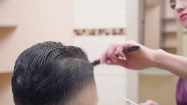 Müşterilerin saçını tarama ustası, yakın çekim. Saç kesme işlemi, berber dükkanında kaydedilmiş. Stilist iş başında. Seçici yumuşak odaklanma. Bulanık arkaplan.