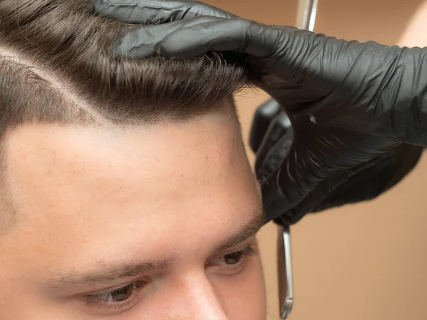 Coiffeur rasage temples clients avec rasoir ouvert, vue rapprochée. Mains stylistes en gants de caoutchouc noir. Photographié au salon de coiffure. Mise au point sélective. Fond flou . — Photo