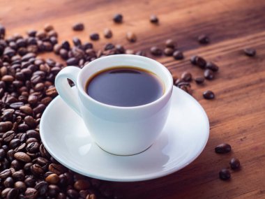 Kahve fincanının siyah espresso ile kompozisyonu ve kahve çekirdekleri kahverengi masaya haplanmış, yakın görüş. Ahşap masa dokusu. Seçici yumuşak odaklanma. Bulanık arkaplan.