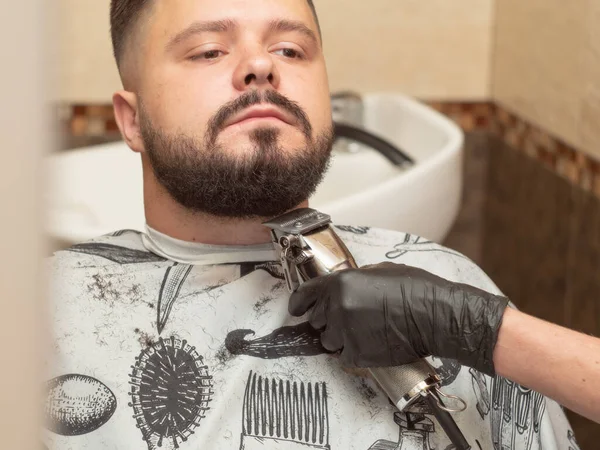 Castor machos de corte con clipper, vista de cerca. Estilistas mano en guante de goma negro. Hombre en la peluquería. Interior del salón de peluquería. Enfoque suave selectivo. Fondo borroso . —  Fotos de Stock