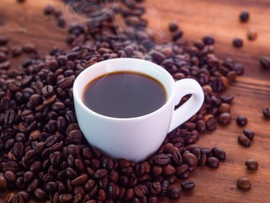 Kahve çekirdekleri aromatik espresso dolu beyaz kahve fincanının etrafına doluşmuş, yakın görüş. Ahşap masa dokusu. Sanat kompozisyonu. Seçici yumuşak odaklanma. Bulanık arkaplan.