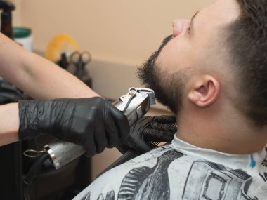 Erkek kunduzları kırpıcı ve tarak ile kesen stilist, görüntüyü kapat. Siyah lastik eldivenli ustalar. Kuaför salonunda fotoğraflanmış. Seçici yumuşak odaklanma. Bulanık arkaplan.