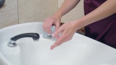 Koyu kırmızı üniformalı stilist ellerini beyaz lavaboda yıkıyor, yakın çekim. Saç stilisti tıraş olmadan önce ellerini yıkıyor, berber dükkanında kaydedilmiş. Kuaför salonunun içi. Seçici yumuşak odak.