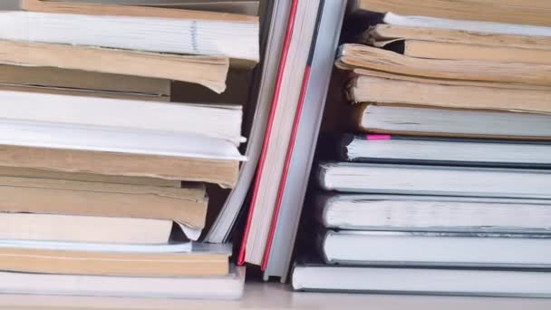 Dolly sliding shot along book shelve. Books randomly stacked on the bookshelf close up. Moving from left to right. Many books piles. — Stock Video