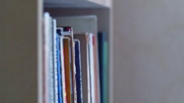 Dolly kitap yığınları boyunca kayar, kitaplık boyunca soldan sağa hareket eder. Farklı yükseklikteki kitaplar yan yana durur. Kitapların çeşitli omurgalarının görüntüsü.