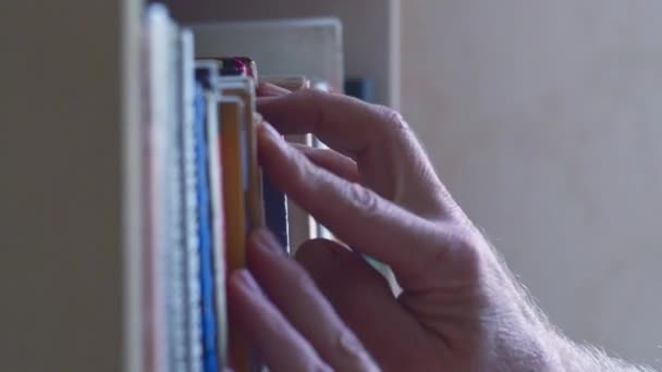 Vista de mãos de homens que escolhem livro na prateleira. Dolly deslizando tiro ao longo de pilhas de livros, movendo-se da esquerda para a direita ao longo da prateleira do livro. Vista das várias espinhas de livros de perto — Vídeo de Stock