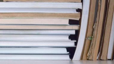 Dolly kitap rafı boyunca kayıyor. Soldan sağa hareket ediyor. Kitaplar ayakta ve istiflenmiş. Kitaplar kitaplıkta, yakın çekimde. Yırtık sayfalı eski kitaplar yenilerinin yanında durur.