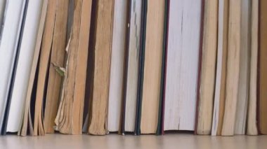 Dolly kitap rafı boyunca kayıyor. Sağdan sola paralel hareket. Kitaplar kitaplıkta, yakın çekimde. Yırtık ve yağlı sayfaları olan eski kitaplar yenilerinin yanında durur..