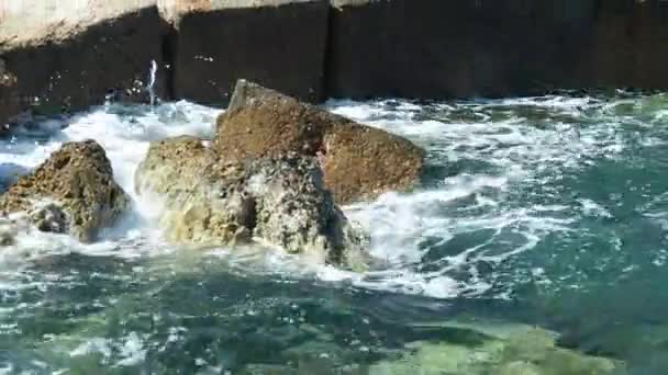 Θαλασσινά κύματα τρέχουν πάνω σε γκρίζες πέτρες, από κοντά. Αφρός θαλάσσης στην επιφάνεια. Φωτογραφήθηκε στην Αίγυπτο το Φεβρουάριο. Επιλεκτική μαλακή εστίαση. Θολή φόντο. — Αρχείο Βίντεο