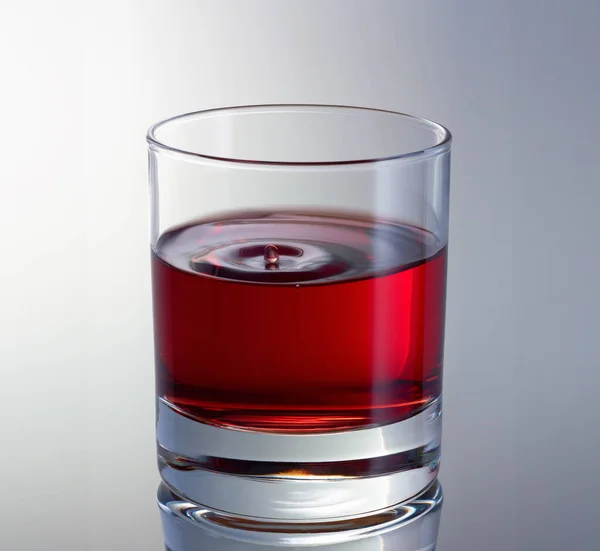Gotejamento gota na superfície do vinho em vidro vista de perto. Gota de vinho tinto com ondas concêntricas — Fotografia de Stock