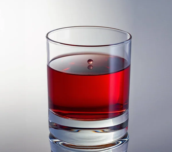 Una goccia di vino che vola sopra la superficie pulita del vino rosso in un bicchiere da vicino. Colpo ad alta velocità. — Foto Stock