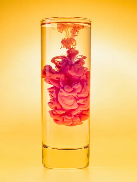 Nube de tinta roja en un vaso de agua. Grabado en estudio. Pintura en agua sobre fondo amarillo. Esquema de color analógico . — Foto de Stock