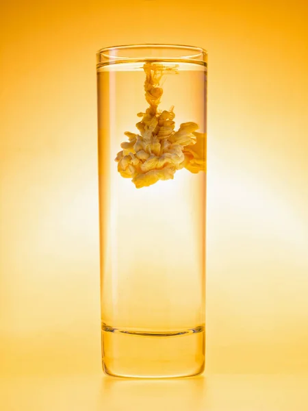 Tinta amarela na água. Abstrato turbilhão nublado em vidro. Esquema monocromático. Conceito de coquetéis criativos — Fotografia de Stock