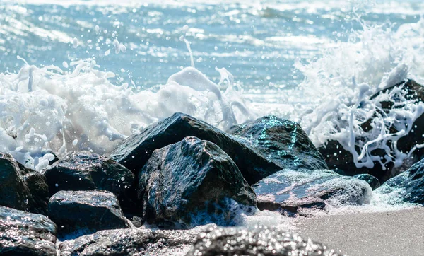 Spritzer Meereswellen auf den schwarzen Steinen im Sand der Bea — Stockfoto