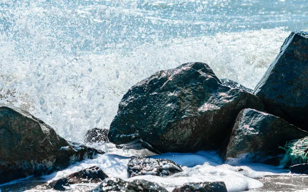 Spritzer Meereswellen auf den schwarzen Steinen im Sand der Bea — Stockfoto