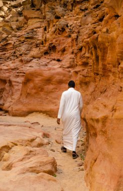 Beyaz Arap elbiseli bir adam Mısır 'da renkli bir kanyonda yürür.