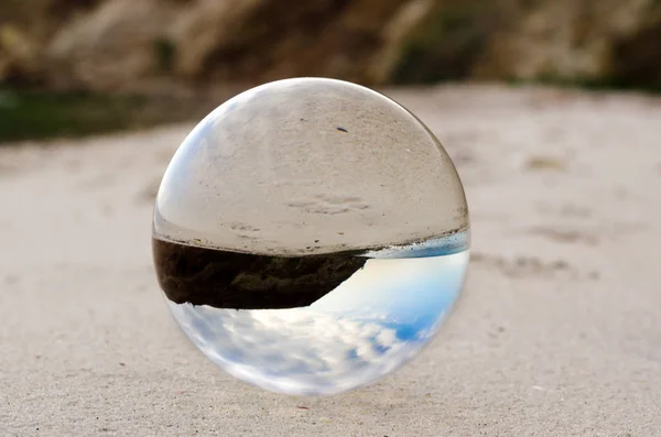 Lente bola de vidrio se encuentra en la arena de la orilla del mar —  Fotos de Stock