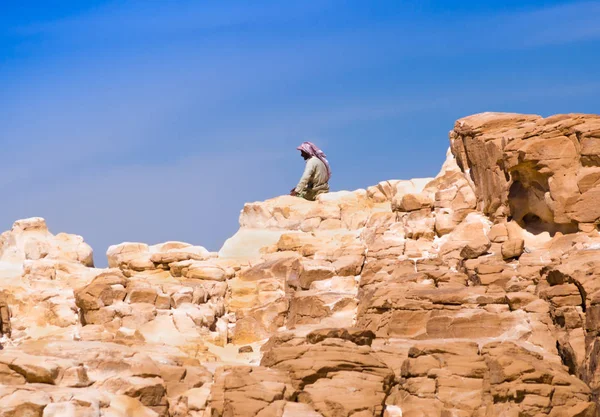 Beduínské sedí na vrcholu vysoké kamenné skále proti modré — Stock fotografie