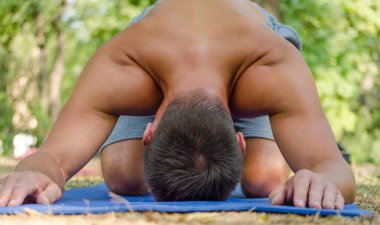 Balasana yogalı genç sporcu mavi bir paspasın üzerinde poz veriyor.