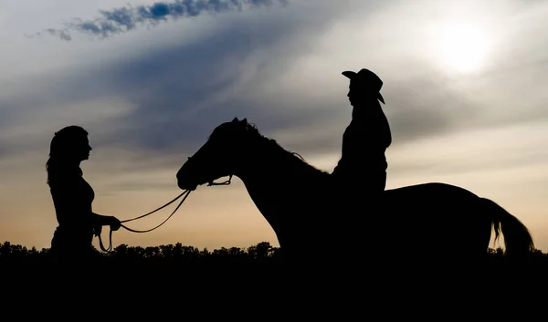Silueta de dos chicas jóvenes con sombrero y caballo en el fondo del atardecer — Foto de Stock
