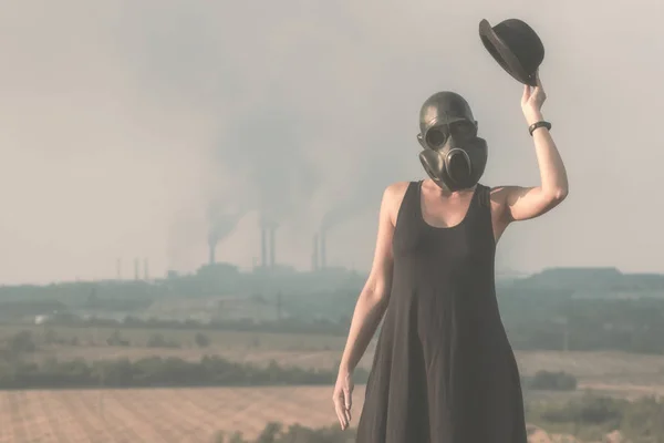 Young girl in a black dress and gas mask on the background of smoking factory chimneys — Stock Photo, Image