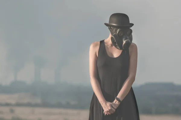 Young girl in a black dress and gas mask on the background of smoking factory chimneys — Stock Photo, Image