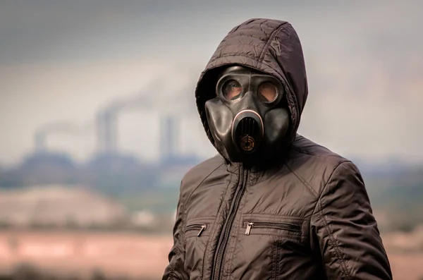 Retrato de un hombre con una máscara de gas y una capucha contra el fondo de humo de las tuberías de la fábrica —  Fotos de Stock