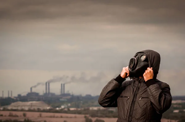One man in a gas mask and a hood amid smoke from factory pipes — Stock Photo, Image