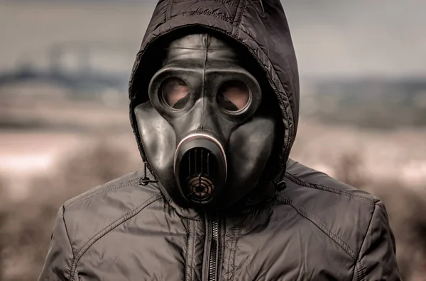 Retrato de un hombre con una máscara de gas y una capucha contra el fondo de humo de las tuberías de la fábrica — Foto de Stock