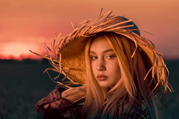 Retrato de una joven con el pelo rubio en un sombrero de paja en la noche al atardecer en verano — Foto de Stock