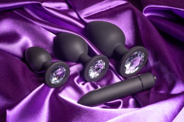 four mismatched silicone black butt plugs with crystals on purple satin fabric