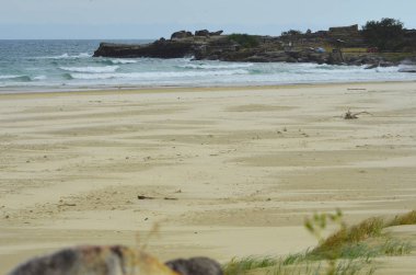 Issız bir kumsal kum bir rock raf mesafe doğru uzanır. Bu çürük var. Bazı otlar ve bir kayanın ön planda olan.