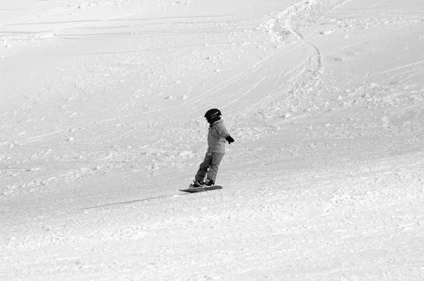 Bir çocuk bir ıssız Kayak-koşmak aşağı snowboard. Yüzlerini bir kask ile kaplı ve uzak açık. Fotoğrafı siyah-beyaz olduğunu.
