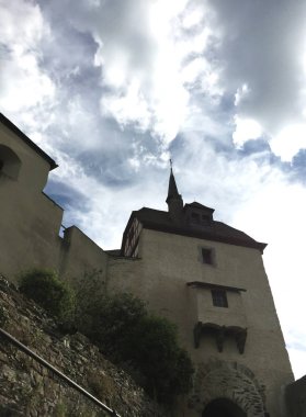Almanya'da bir kale kule bulutlu bir gökyüzüne yükselir. Bir rüzgar vane taretin olan kule kaç pencere vardır. Bir tuğla duvar ön planda olduğunu.